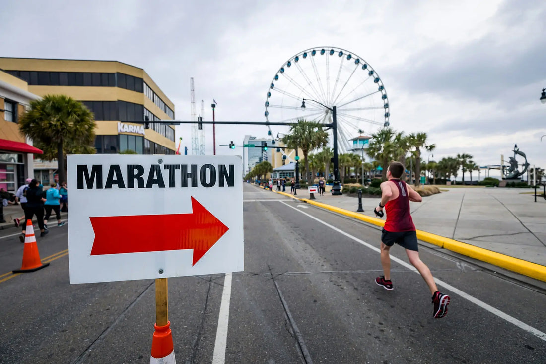 Lady running a marathon, past a sign saying marathon. Big wheel in the background