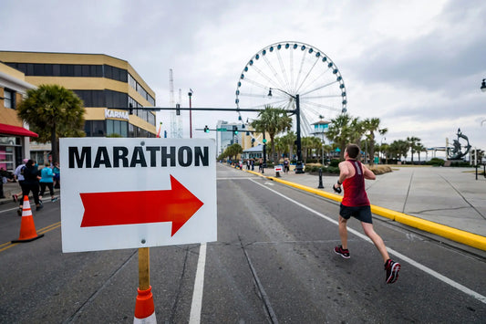Lady running a marathon, past a sign saying marathon. Big wheel in the background
